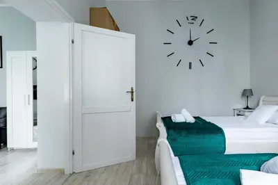 a white bedroom with a bed and a clock on the wall at Wawel Castle Apartment in Kraków