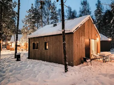 a wooden cabin with a snow covered roof in the snow at La Playa Resort & Camp Trzebinia in Trzebinia