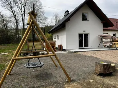 a swing set in front of a white house at Domek całoroczny Zagroda MłyńSKI in Sułkowice