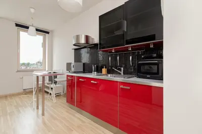 a kitchen with red cabinets and a table with a microwave at Lea Apartments Kraków Krowodrza by Noclegi Renters in Kraków