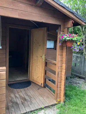 a wooden dog house with a door and flowers at Domek drewniany in Podzamcze