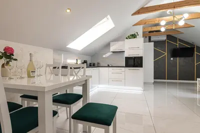 a white kitchen with a table and green chairs at Bianco Apartamenty Laskowa - Zator in Zator