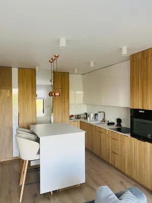 a kitchen with a white counter and wooden cabinets at Luxury White Apartment in Park Lotników in Kraków