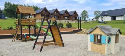a playground with a wooden swing set and a house at Wycisznia - drewniane domki całoroczne in Gierałtowiczki