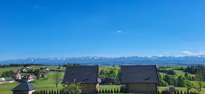 a group of houses on a hill with mountains in the background at Domki Na Grapie - z widokiem na Tatry in PyzÃ³wka