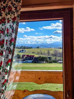 a window with a view of a field and mountains at Domki Na Grapie - z widokiem na Tatry in PyzÃ³wka