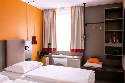 a bedroom with two beds and a desk and a window at Vienna House Easy by Wyndham Cracow in Kraków