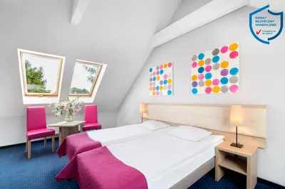 a bedroom with a bed and two pink chairs at Hotel Petrus in Kraków