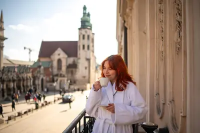 a woman standing on a balcony drinking a cup of coffee at Hotel Senacki in Kraków