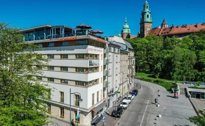 a white building on a city street with cars parked at Hotel Pod Wawelem in Kraków