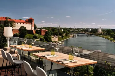 a balcony with tables and chairs with a view of a river at Sheraton Grand Krakow in Kraków