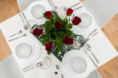 a table with white plates and a vase of red roses at Szpitalna Premium Apartment in Kraków