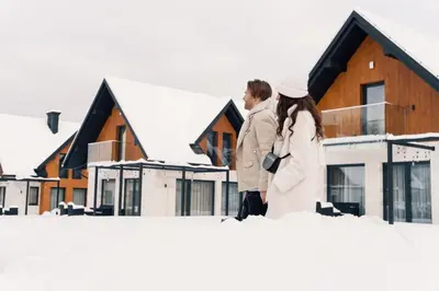 two people standing in the snow in front of houses at Dolina Barw - całoroczne domki na wynajem in Rabka
