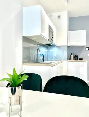 a kitchen with white cabinets and a table and chairs at Modern Green Apartment in Kraków
