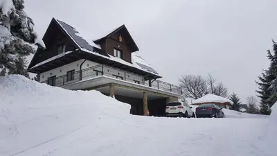 a house covered in snow with cars parked in front at Willa pod Babią Górą in Zubrzyca Górna