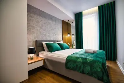 a bedroom with a bed with green sheets and a window at Capital apartaments in Zator