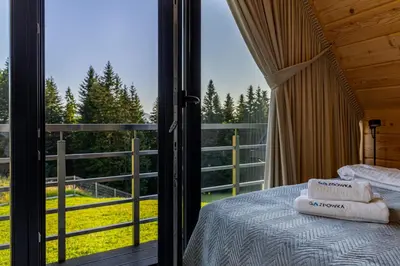 a bedroom with a bed and a balcony with a view at Kompleks Gazdówka - Domki Rabka-Zdrój in Ponice