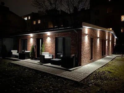 a brick building with a group of chairs on a patio at night at Sander Apartments in Kraków