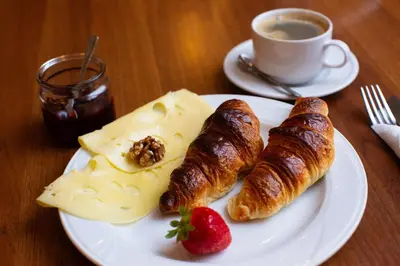 a plate of food with croissants and cheese and a cup of coffee at David Boutique ApartHotel in Kraków