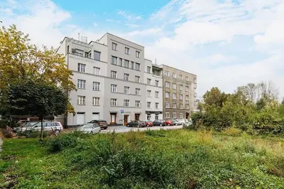 a large white building with cars parked in a parking lot at Urocze mieszkanie w krakowskiej kamienicy in Kraków