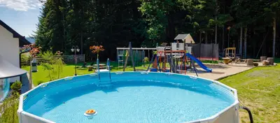 a large blue pool in a yard with a playground at Domki Pod Lasem MM in Rabka