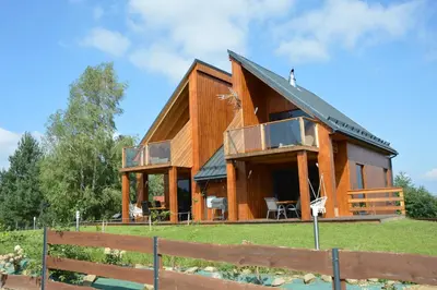 a large wooden house with a balcony on a field at Tarnawa Gold, Sauna, Jacuzzi, Grota solna, in Tarnawa Dolna