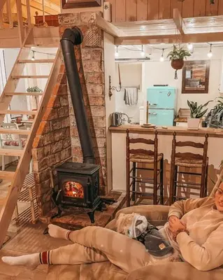 a man sitting on a couch in a living room with a stove at Ojcowski Zakątek-domek z balią oraz drewniany domek do wynajęcia in Wola Kalinowska