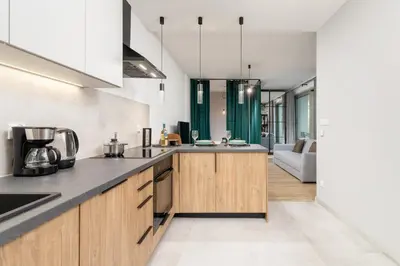 a kitchen with wooden cabinets and a living room at Kraków Rynek Podgórski Apartment by Noclegi Renters in Kraków