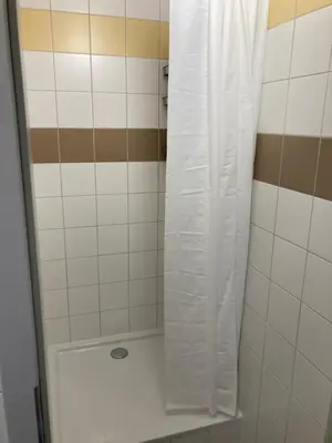 a shower with a white shower curtain in a bathroom at Hostel przy Stadionie in Jaworzno