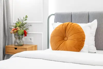 a bed with an orange pillow and a vase of flowers at HOUSEHOST Apartment: Św.Gertrudy 10/2.11 in Kraków