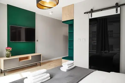 a bedroom with a green accent wall and a bed with towels at HOUSEHOST Apartament :Miodowa 42/4b in Kraków