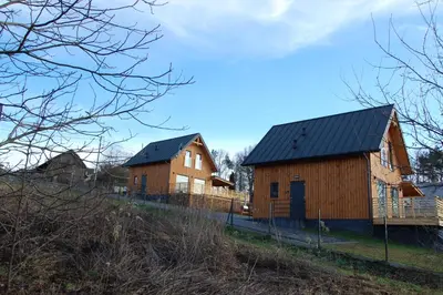 two barns with black roofs on a hill at Sielski Zakątek Dąbrówka Domki in Dąbrówka