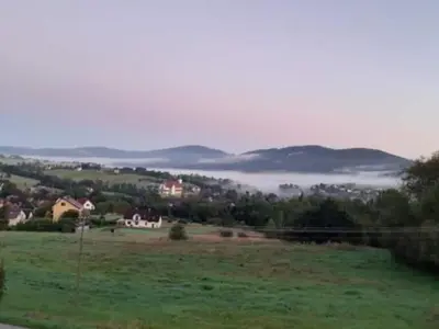a green field with a town in the distance with a foggy valley at POD RÓŻĄ in Kasina Wielka