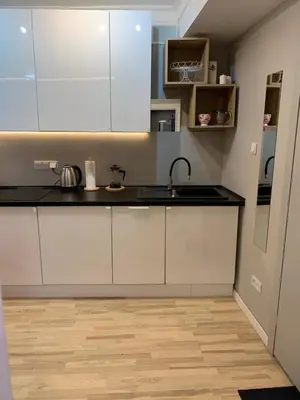 a kitchen with white cabinets and a wooden floor at Petit Appartement in Kraków
