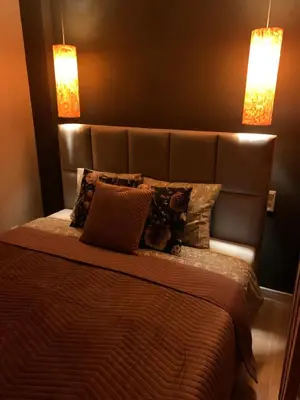 a bedroom with a bed with a leather headboard and two lights at Petit Appartement in Kraków