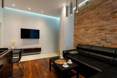 a living room with a black leather couch and a brick wall at Luna Prestige Suite - Old Town Center & Main Station in Kraków