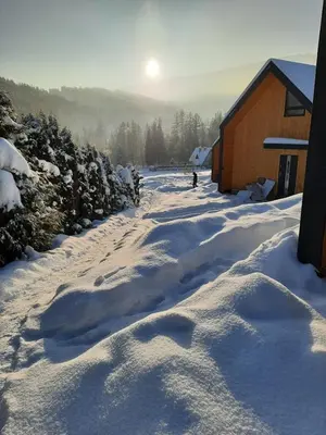 a snow covered road next to a building with the sun in the background at Beskidzkie Super Stodoły in Zawoja