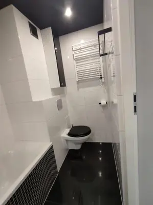 a white bathroom with a toilet with a black seat at Przytulne mieszkanko in Oświęcim