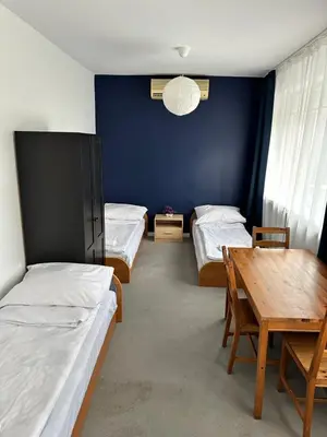 a room with three beds and a wooden table at Hostel Demi in Kraków